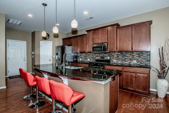 kitchen with appliances with stainless steel finishes, dark hardwood / wood-style flooring, decorative light fixtures, a breakfast bar area, and a center island with sink