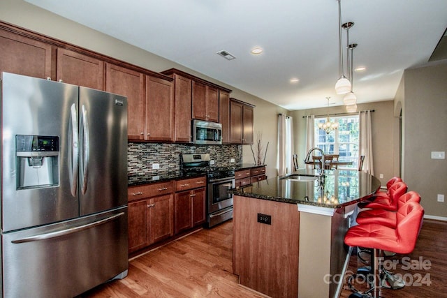 kitchen with appliances with stainless steel finishes, a kitchen island with sink, light hardwood / wood-style flooring, sink, and decorative light fixtures