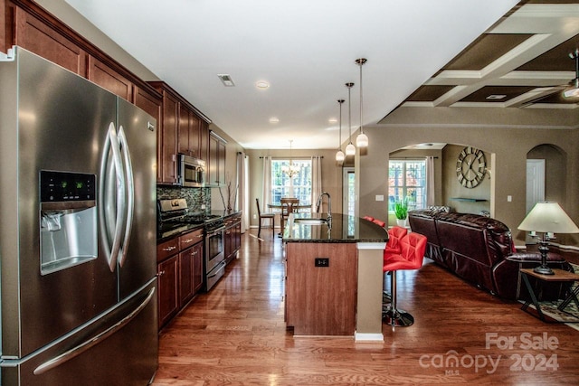 kitchen with sink, an island with sink, a kitchen breakfast bar, stainless steel appliances, and dark wood-type flooring