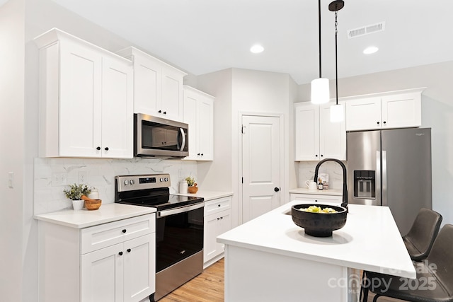 kitchen featuring appliances with stainless steel finishes, decorative light fixtures, white cabinetry, a kitchen island, and a breakfast bar area