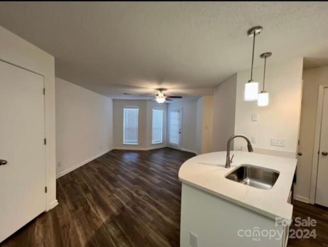 kitchen with sink, a textured ceiling, kitchen peninsula, hanging light fixtures, and dark wood-type flooring