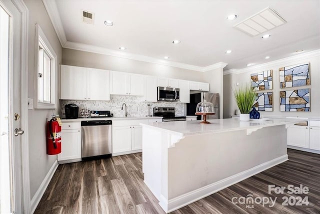 kitchen with a kitchen island, appliances with stainless steel finishes, white cabinetry, dark wood-type flooring, and crown molding