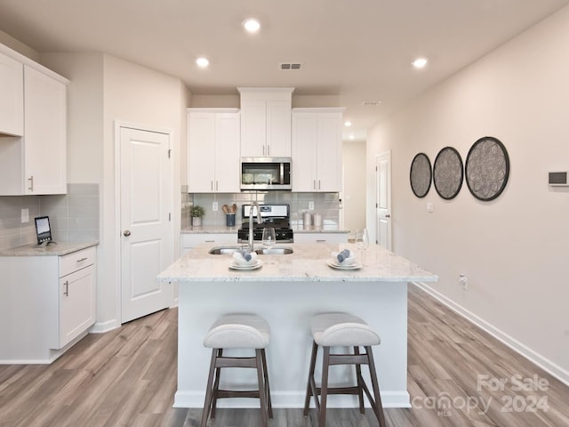 kitchen with a center island with sink, light hardwood / wood-style flooring, appliances with stainless steel finishes, tasteful backsplash, and white cabinetry