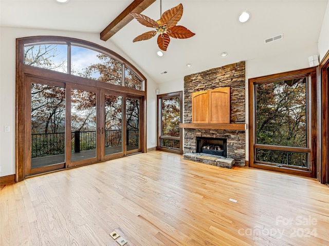 unfurnished living room featuring lofted ceiling with beams, ceiling fan, a stone fireplace, and light hardwood / wood-style floors