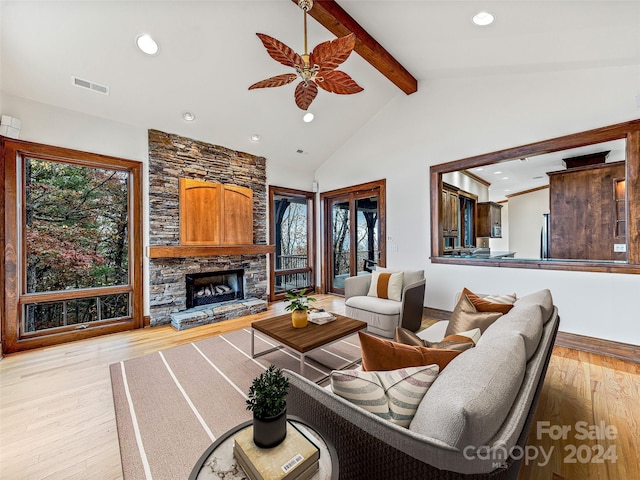 living room featuring high vaulted ceiling, beamed ceiling, ceiling fan, a fireplace, and light hardwood / wood-style flooring