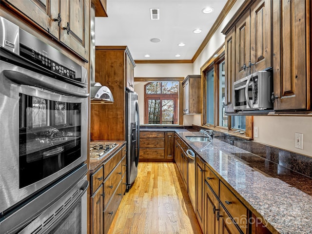 kitchen featuring light hardwood / wood-style floors, dark stone counters, sink, crown molding, and appliances with stainless steel finishes