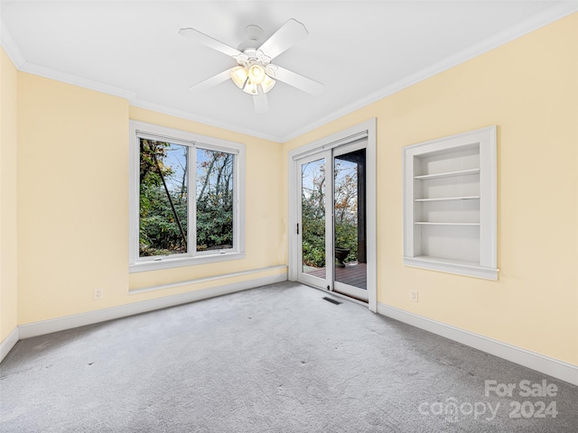 carpeted spare room featuring ornamental molding, built in shelves, and ceiling fan