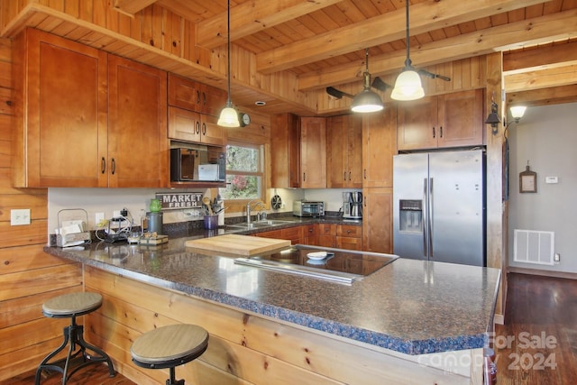 kitchen featuring hanging light fixtures, stainless steel fridge, beam ceiling, a breakfast bar area, and dark hardwood / wood-style floors