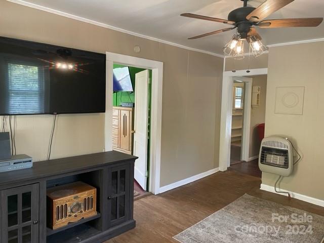 unfurnished living room featuring ornamental molding, ceiling fan, heating unit, and dark hardwood / wood-style flooring