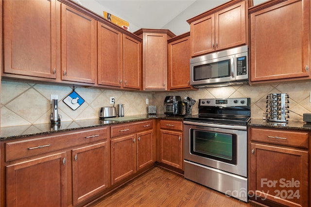 kitchen featuring dark stone countertops, backsplash, stainless steel appliances, and wood-type flooring