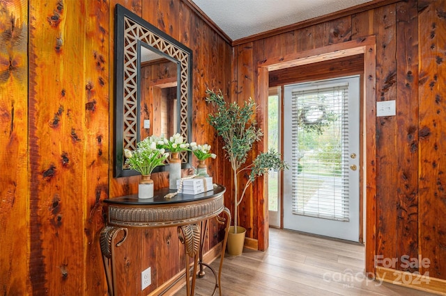 foyer with crown molding, wood walls, a textured ceiling, and light hardwood / wood-style flooring