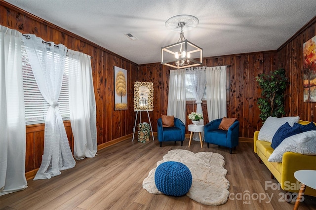 living area featuring a notable chandelier, wood walls, wood finished floors, visible vents, and ornamental molding