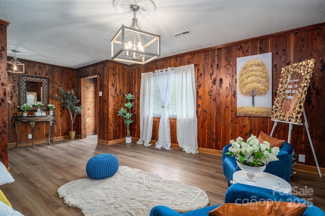 living area featuring a textured ceiling, wood finished floors, visible vents, baseboards, and crown molding