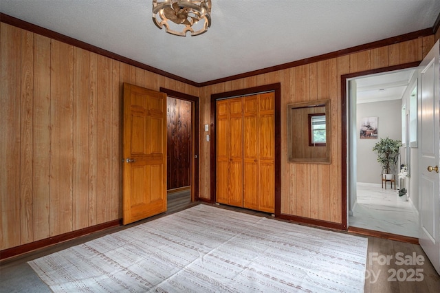 unfurnished bedroom featuring light wood-type flooring, a closet, wood walls, and baseboards