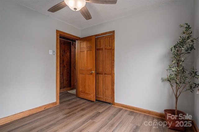 spare room with a textured ceiling, ceiling fan, light wood-style flooring, and baseboards