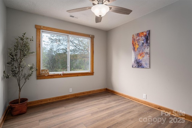 unfurnished room featuring light wood finished floors, visible vents, a ceiling fan, a textured ceiling, and baseboards