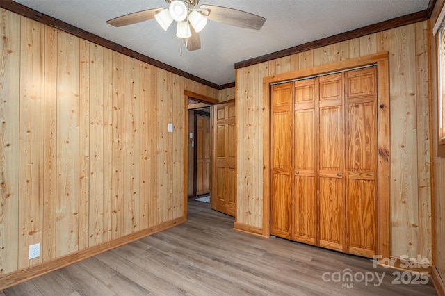 unfurnished bedroom with baseboards, a textured ceiling, wood walls, light wood-style floors, and a closet