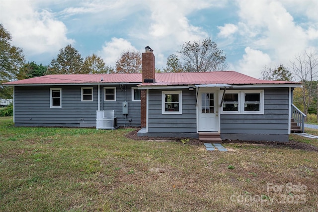 rear view of house with entry steps, a chimney, metal roof, and a yard