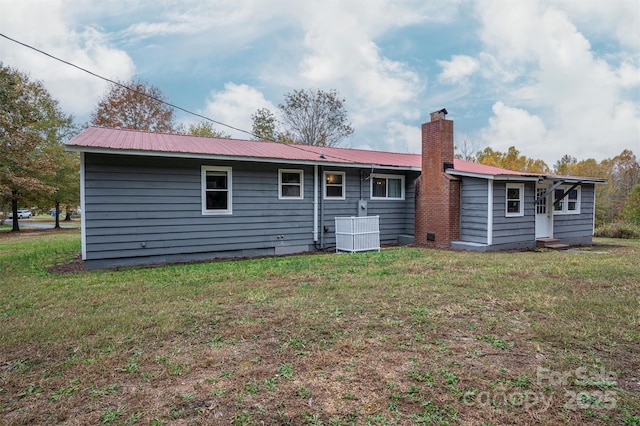 rear view of property featuring entry steps, a chimney, metal roof, and a yard