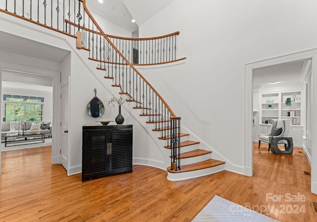 stairway featuring high vaulted ceiling, wood-type flooring, and ornamental molding