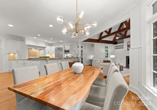 dining space with beamed ceiling, ornamental molding, and light hardwood / wood-style floors