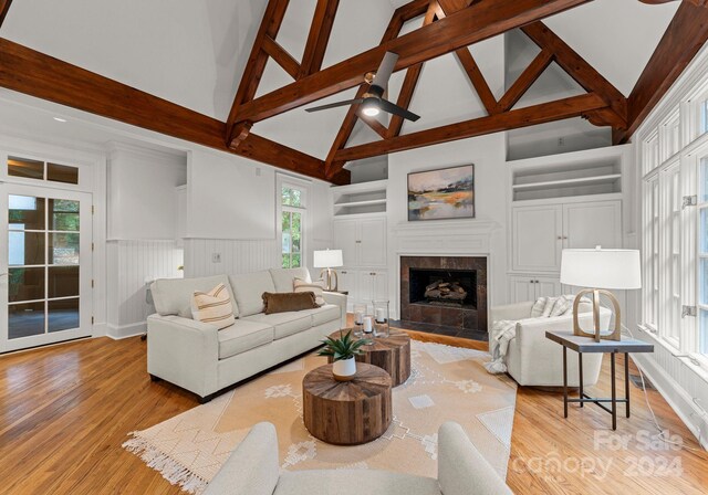 living room featuring built in features, ceiling fan, beam ceiling, high vaulted ceiling, and light hardwood / wood-style flooring