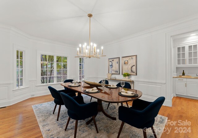 dining space with light hardwood / wood-style flooring, ornamental molding, and a notable chandelier