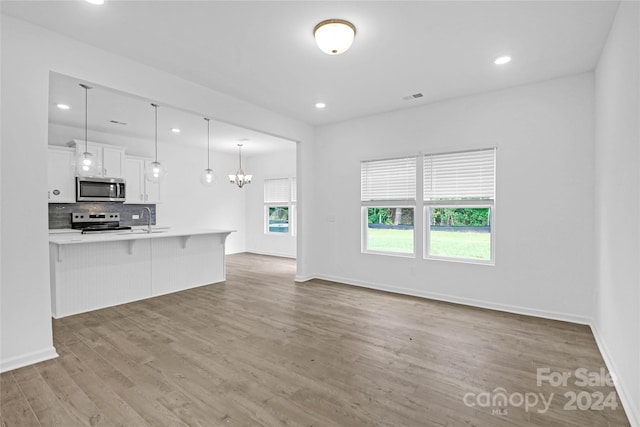 unfurnished living room with plenty of natural light, wood-type flooring, sink, and an inviting chandelier