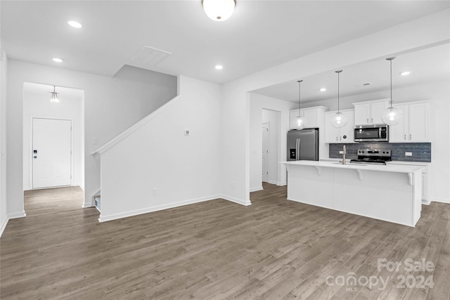 kitchen featuring decorative backsplash, an island with sink, appliances with stainless steel finishes, decorative light fixtures, and white cabinetry