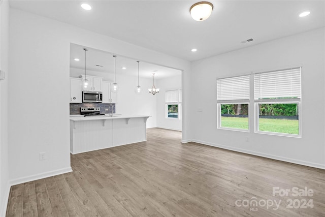 kitchen with stainless steel appliances, pendant lighting, white cabinets, light hardwood / wood-style floors, and a breakfast bar area