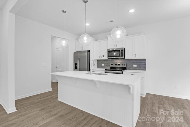 kitchen with sink, hanging light fixtures, stainless steel appliances, a kitchen island with sink, and white cabinets