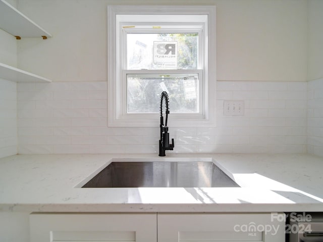 interior details with sink, white cabinets, and light stone counters