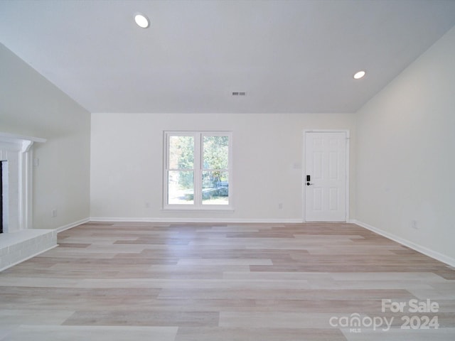 unfurnished living room with vaulted ceiling, light hardwood / wood-style flooring, and a fireplace