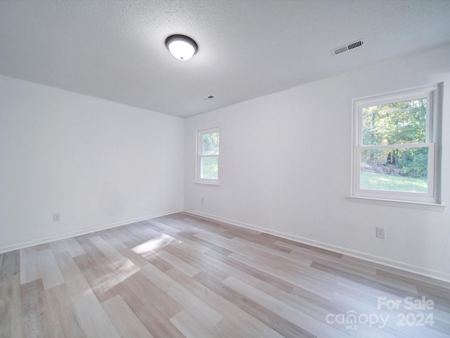 spare room with light hardwood / wood-style flooring, a textured ceiling, and a healthy amount of sunlight