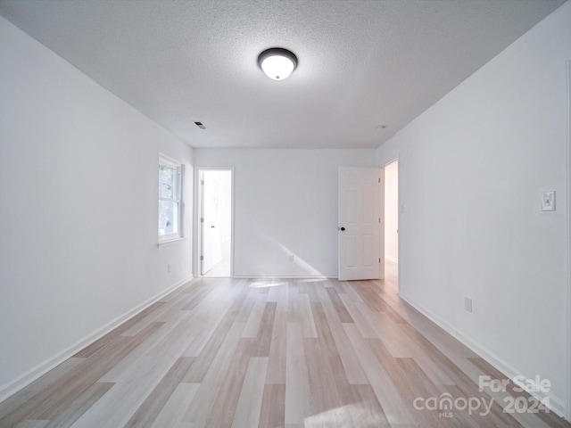 unfurnished room with a textured ceiling and light wood-type flooring