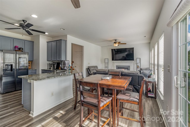 kitchen featuring gray cabinetry, dark stone counters, dark hardwood / wood-style floors, and stainless steel fridge with ice dispenser