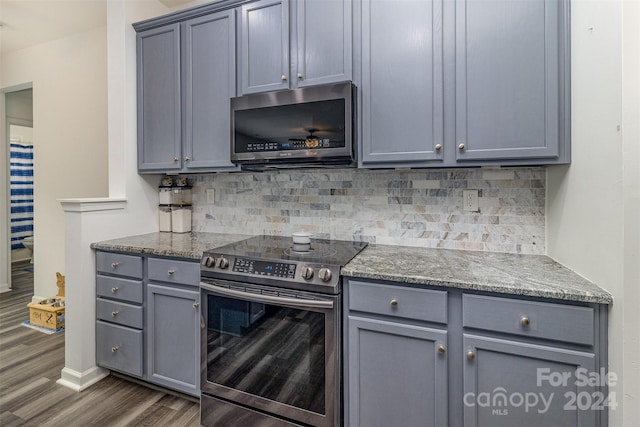 kitchen with tasteful backsplash, gray cabinetry, dark stone counters, appliances with stainless steel finishes, and dark hardwood / wood-style floors