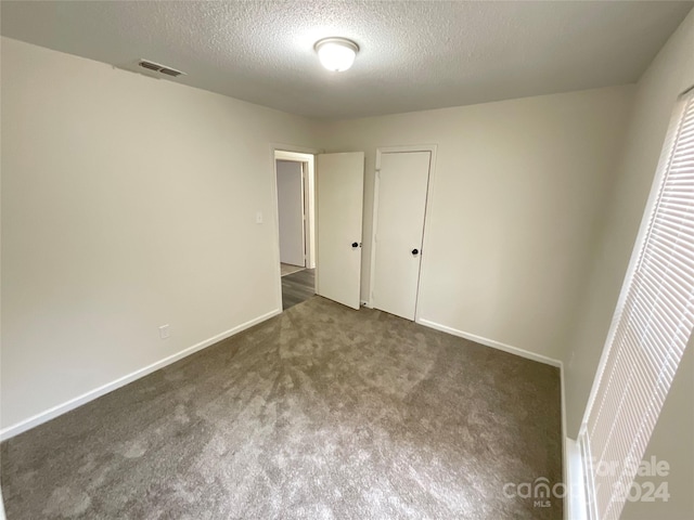 unfurnished bedroom with dark colored carpet, a textured ceiling, and a closet