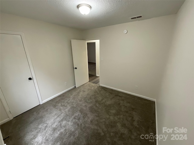 spare room with a textured ceiling and dark colored carpet