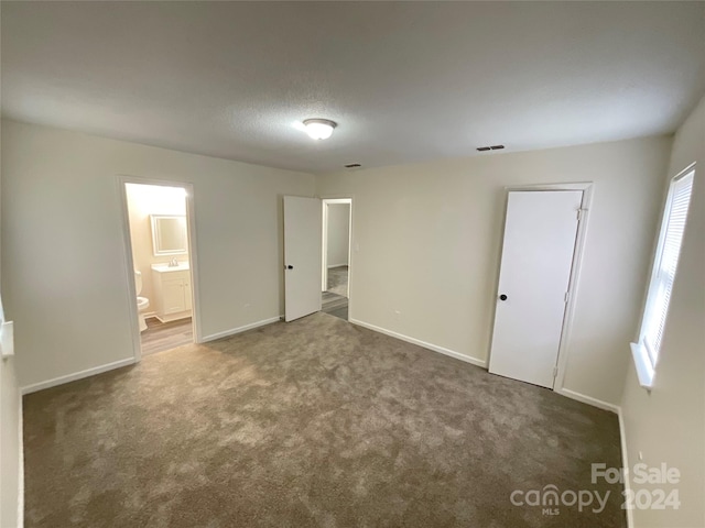 unfurnished bedroom featuring ensuite bathroom, a closet, and dark carpet