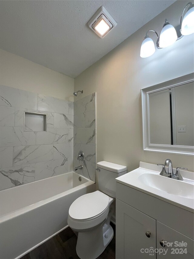 full bathroom featuring wood-type flooring, toilet, tiled shower / bath, a textured ceiling, and vanity