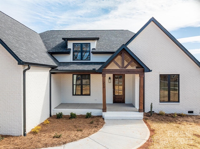 view of exterior entry with a porch, brick siding, and a shingled roof