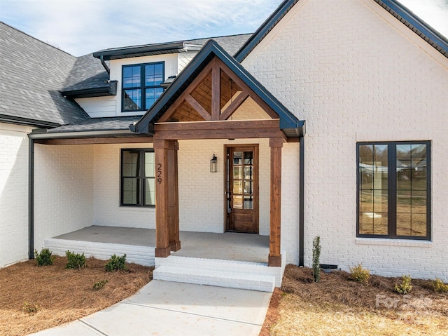 entrance to property with covered porch, roof with shingles, brick siding, and crawl space