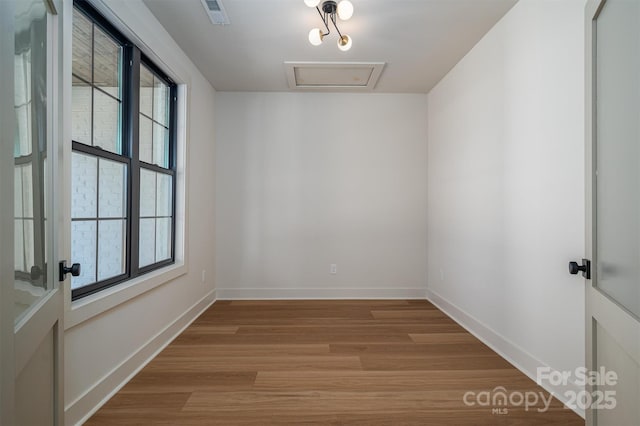 unfurnished room featuring attic access, wood finished floors, visible vents, and baseboards