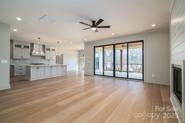 unfurnished living room featuring a large fireplace, ceiling fan, light wood finished floors, and recessed lighting