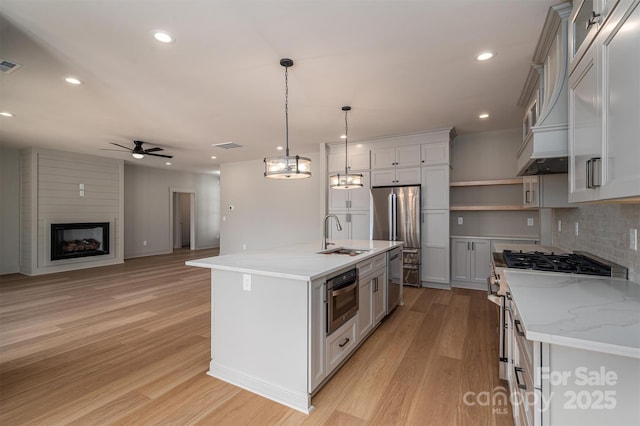 kitchen featuring appliances with stainless steel finishes, light wood-style floors, a fireplace, open shelves, and a sink