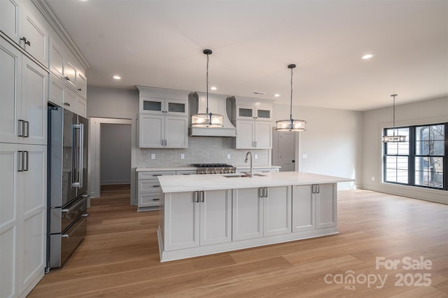 kitchen with high quality fridge, premium range hood, a sink, light countertops, and tasteful backsplash