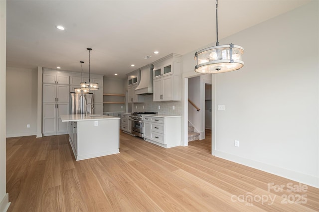 kitchen with light wood finished floors, light countertops, custom range hood, decorative backsplash, and appliances with stainless steel finishes