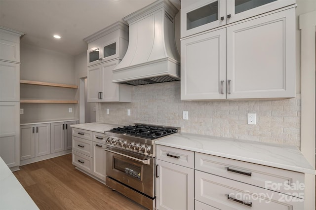 kitchen featuring stainless steel range, custom range hood, light wood-style flooring, glass insert cabinets, and light stone countertops