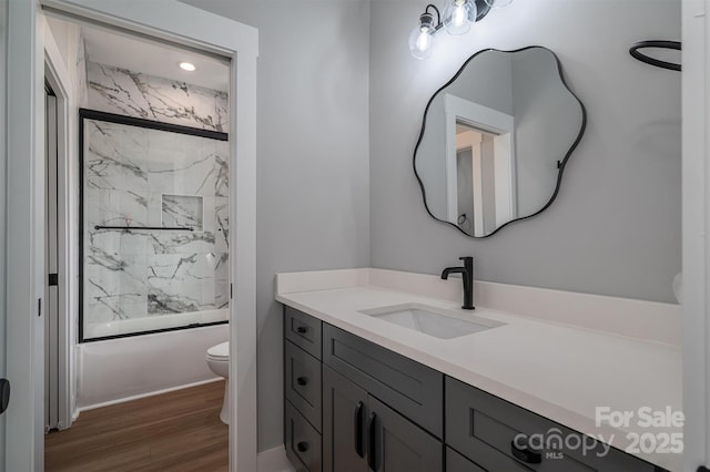 full bathroom featuring wood finished floors, shower / bath combination with glass door, vanity, and toilet